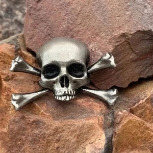 Vintage silver skull and crossbones brooch pin with a distressed finish on rock background