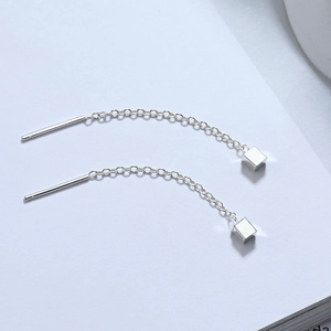 Detail of s925 silver threader earrings with minimalist cube charms on white surface