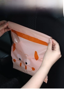 Adhesive car trash bag with pink cartoon pig design being attached to the seat back