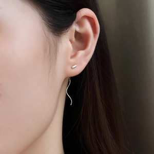 Macro shot of minimalist silver S-shaped wave tassel earring worn by a model