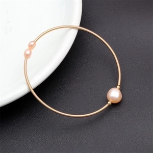 Macro shot of gold wire wrap bracelet featuring three pink freshwater pearls on white ceramic