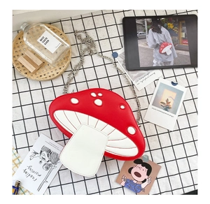 Close-up of red and white mushroom crossbody bag with silver chain on picnic cloth