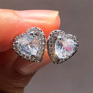 Detailed macro view of heart-shaped zircon earrings with pavé halo setting held by hand