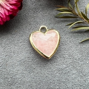 Detail of a pink crystal heart pendant with a gold frame on a grey velvet surface