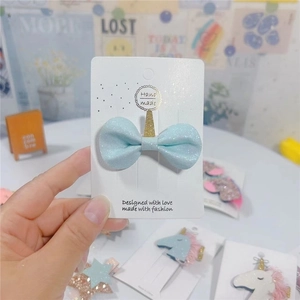 Detail of light blue glitter hair bow featuring a golden unicorn horn on a display card