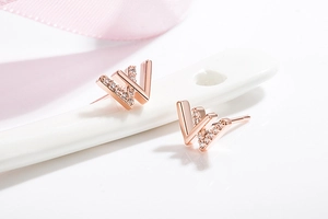 Detailed macro view of rose gold W-shaped stud earrings with sparkling zircon inlay