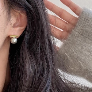 Minimalistische Perlenohrstecker mit goldenem Stab, getragen von einem Model