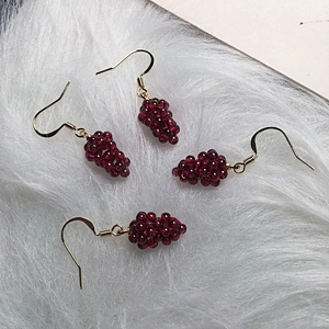 Detailed view of handmade burgundy garnet grape cluster earrings on white fur