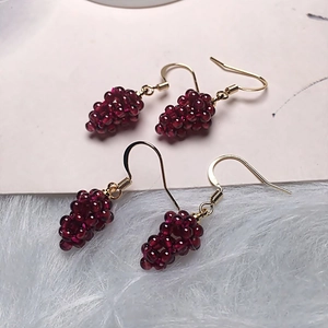 Handmade burgundy garnet grape-shaped earrings with gold hooks on white fur background