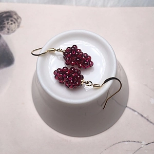 Detailed view of handmade burgundy garnet grape cluster earrings with gold hooks on white ceramic