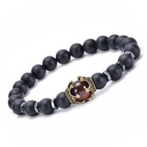 Macro detail of elastic beaded bracelet with matte black onyx and bronze crown charm