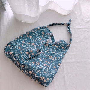 Detail of floral cotton handbag with knotted strap design on a textured white background