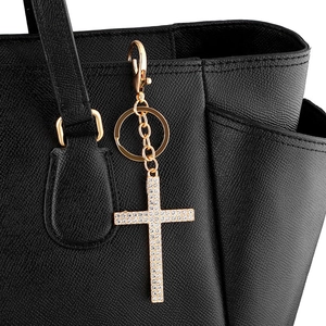 Elegant gold crystal cross keychain with rhinestones attached to a black leather bag