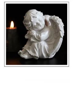 Détail de statue d'ange blanc en résine avec ailes ciselées et lueur de bougie chaude