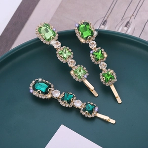 Elegant gold hair clips with green gemstones and white rhinestones on a decorative plate