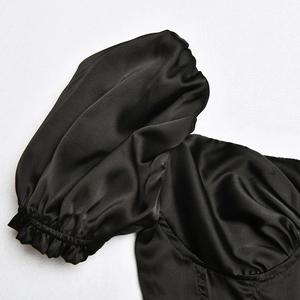 Detailed close-up of glossy black satin fabric and puffy sleeve design on a deep V-neck dress
