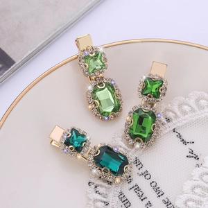 Three emerald green crystal hair clips with gold metal base on a decorative gold plate