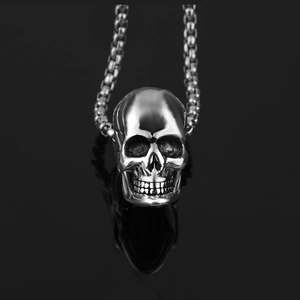 Detailed close-up of a silver skull pendant with box chain on a black reflective surface