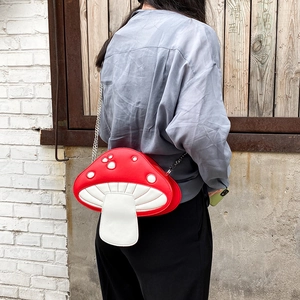Cute red mushroom shaped PU leather crossbody bag with silver chain strap worn outdoors
