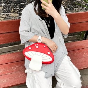 Outdoor shot of a cute red and white mushroom-shaped crossbody bag with a silver chain