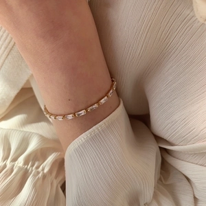 Detail of elegant gold bracelet with rectangular AAA zircons on soft cream fabric