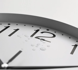 Close-up of minimalist white wall clock with water droplets showing waterproof feature