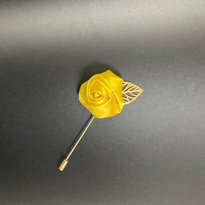 Macro detail of a handmade yellow satin rose lapel pin with a hollow golden leaf accessory