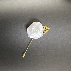 Detail of white fabric rose boutonniere with golden hollow leaf and long metal pin