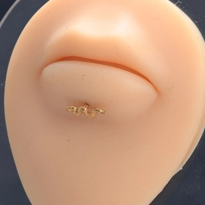 Golden snake-shaped stainless steel labret stud piercing displayed on a lip model