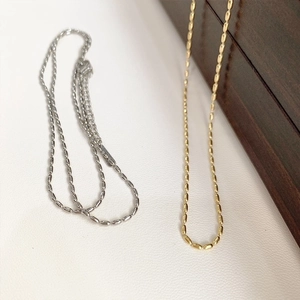 Minimalist 18K gold and silver rice bead necklaces displayed on a wooden jewelry box
