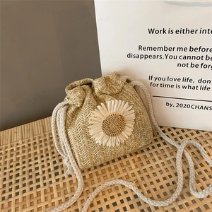 Detail of hand-woven straw bucket bag with white daisy applique and cotton drawstring closure