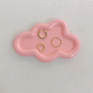 Detailaufnahme von Goldring und Ohrmanschetten auf rosa wolkenförmiger Schmuckschale