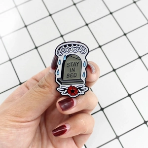 Enamel tombstone badge with flowers and Stay In Bed text held against white background