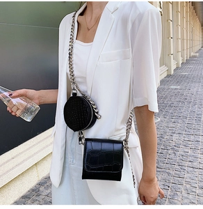 Detail of black crocodile texture composite bag with silver chain strap on white suit