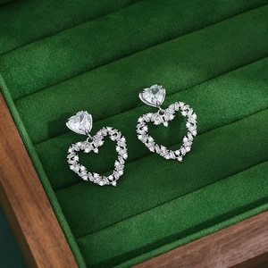 Macro shot of silver heart earrings with sparkling cubic zirconia on green velvet