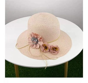 Close-up of pink straw sun hat with detailed fabric flower accents on a white table