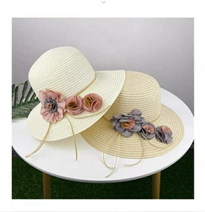 Detail view of woven straw sun hats with floral fabric decorations on white table