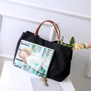 Close-up of minimalist black canvas tote bag featuring premium brown leather handles