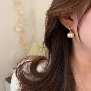 Detail of elegant gold U-shaped earring with a large champagne pearl on a model