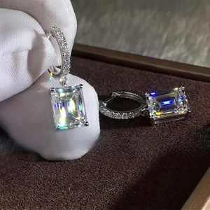 Elegant emerald cut zircon drop earrings in silver setting held by gloved hand
