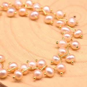Detail of pink freshwater pearls woven with gold metal wire on a wooden surface
