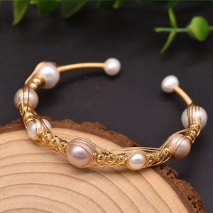 Detail of handmade gold plated woven bracelet with natural pearls on a wood base