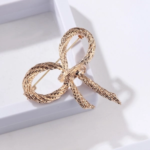 Macro view of gold rope-textured bow brooch with elegant metallic finish and glossy details