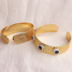Bracelet jonc ouvert doré avec motif œil maléfique et texture rainurée sur tissu