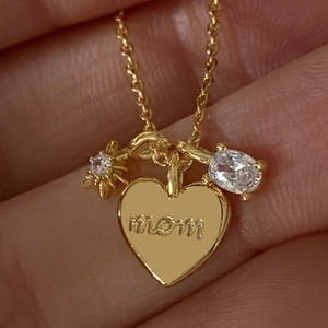 Gold Mom heart necklace with star and oval zircon charms on skin background