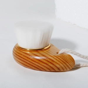 Detail of wooden facial brush with white fibers, gold metal ring, and beige cotton cord