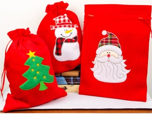 Detailed view of red velvet Christmas gift bags with Santa, snowman, and tree embroidery