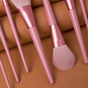 Detailed close-up of premium pink makeup brushes on a textured warm brown surface
