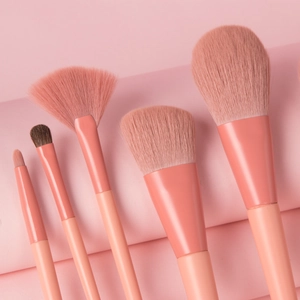 Macro detail of five coral pink makeup brushes with soft bristles on textured paper
