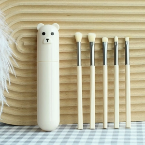 Detailed view of 5-piece beige makeup brush set with cute bear lid storage tube on wood tray
